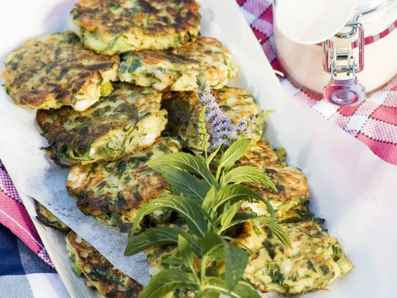 Gestapelte, goldbraune Zucchini Frikadellen, garniert mit frischen Kräutern und lila Blüten. Ein köstlicher Sommergenuss.