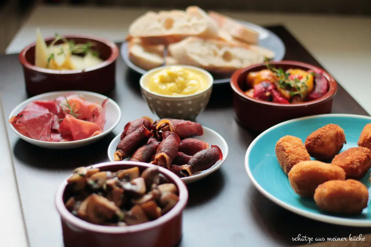 Vielfalt an Tapas: Käse, Schinken, Pilze, gefüllte Datteln im Speckmantel, Kroketten und Brot. Ein Fest für die Sinne!