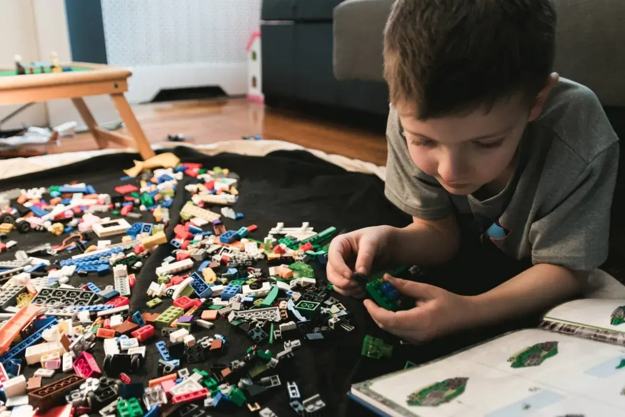 Chłopiec buduje z klocków LEGO, a obok leży instrukcja. Jak umyć klocki LEGO? Wystarczy je zebrać i umyć.