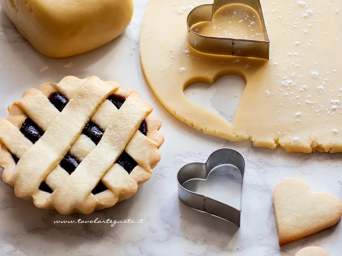 Pasta frolla pronta per essere infornata. La temperatura di cottura è fondamentale per ottenere un risultato perfetto. Cuoricini di frolla e crostata con marmellata.