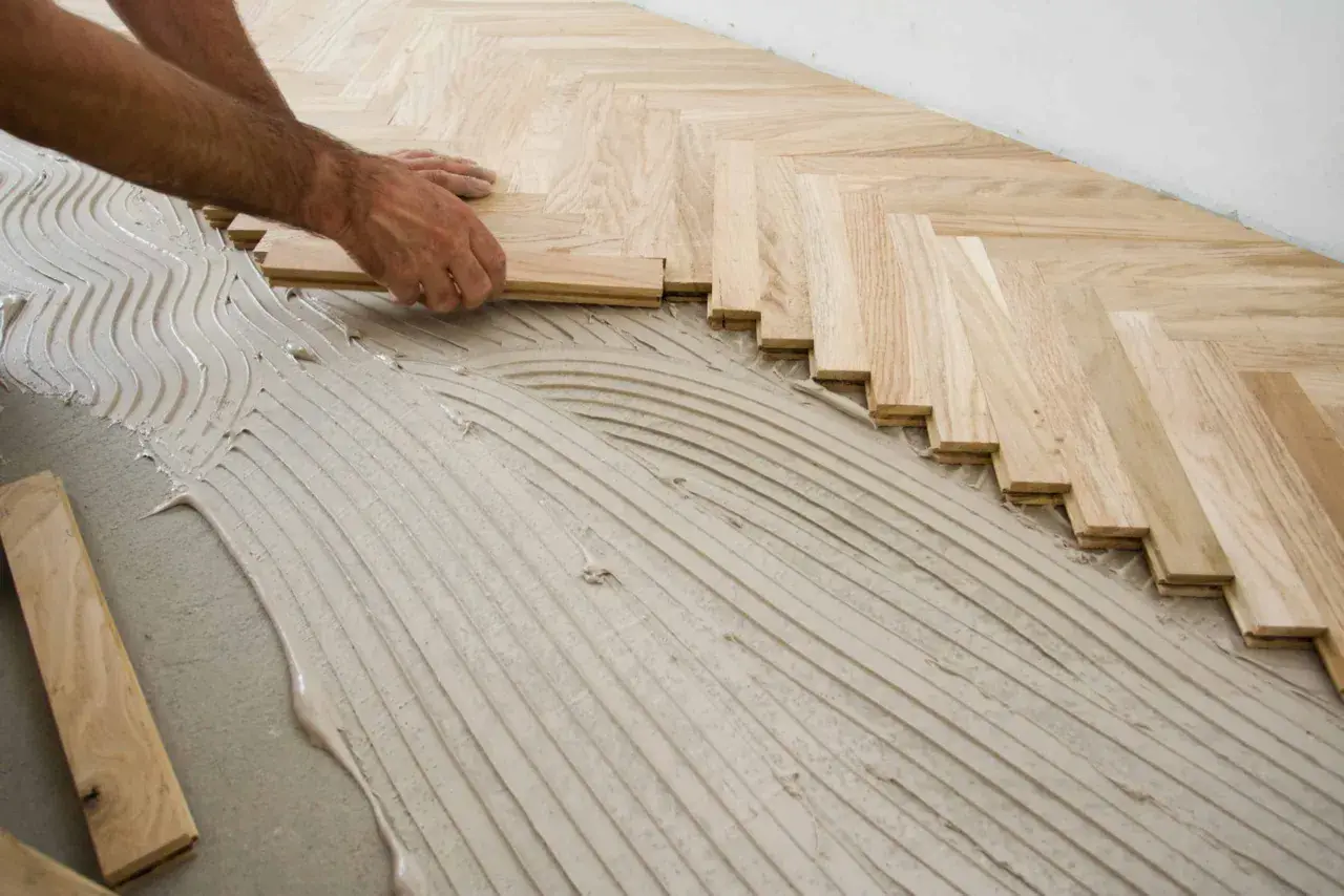 Pose de parquet en chevrons. Des lames de bois clair sont posées sur un lit de colle ondulée.