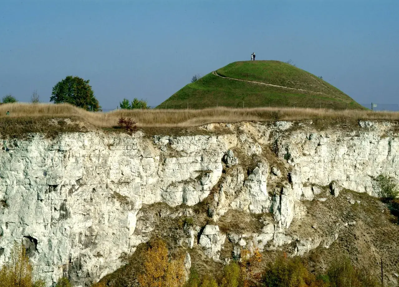 Krakus mound, zielona kopuła z dwiema postaciami na szczycie, góruje nad wapiennym klifem.