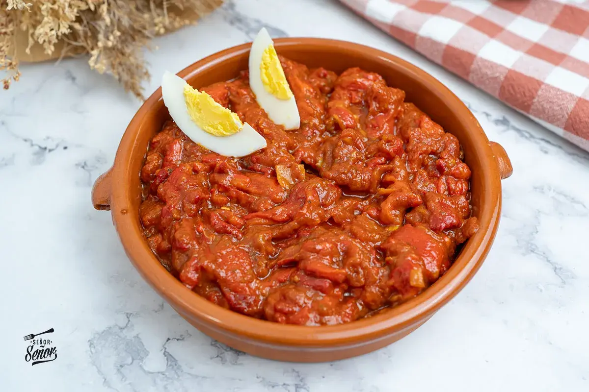 Un plato de asadillo manchego, con pimientos rojos guisados y adornado con gajos de huevo cocido.