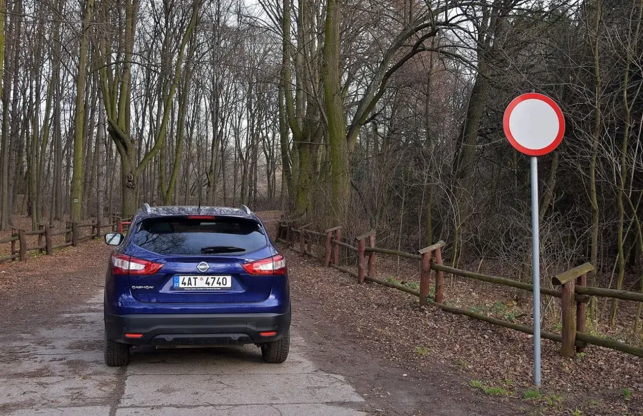 Niebieski Nissan na leśnej drodze, obok znak zakazu ruchu. Kierowca ryzykował wjazd pod zakaz ruchu, mandat murowany.