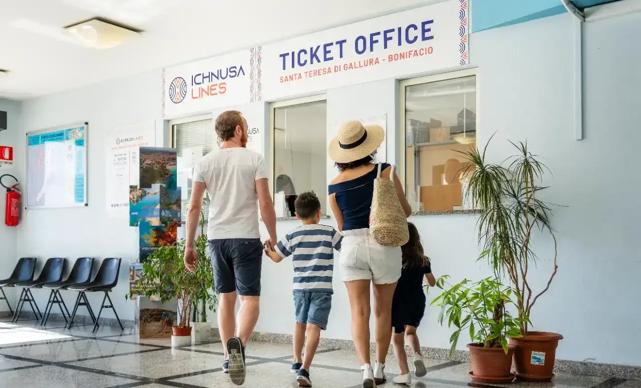 Famiglia in coda all'ufficio biglietti per la Corsica con bambini. L'avventura inizia qui!