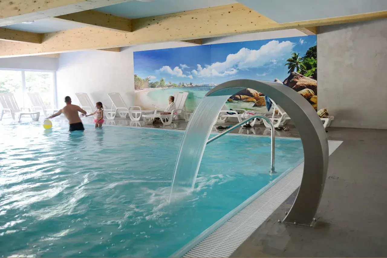 Rodzina bawi się w basenie z wodospadem w hotelu Pokrzywna. Relaks w gorzelnianym klimacie.