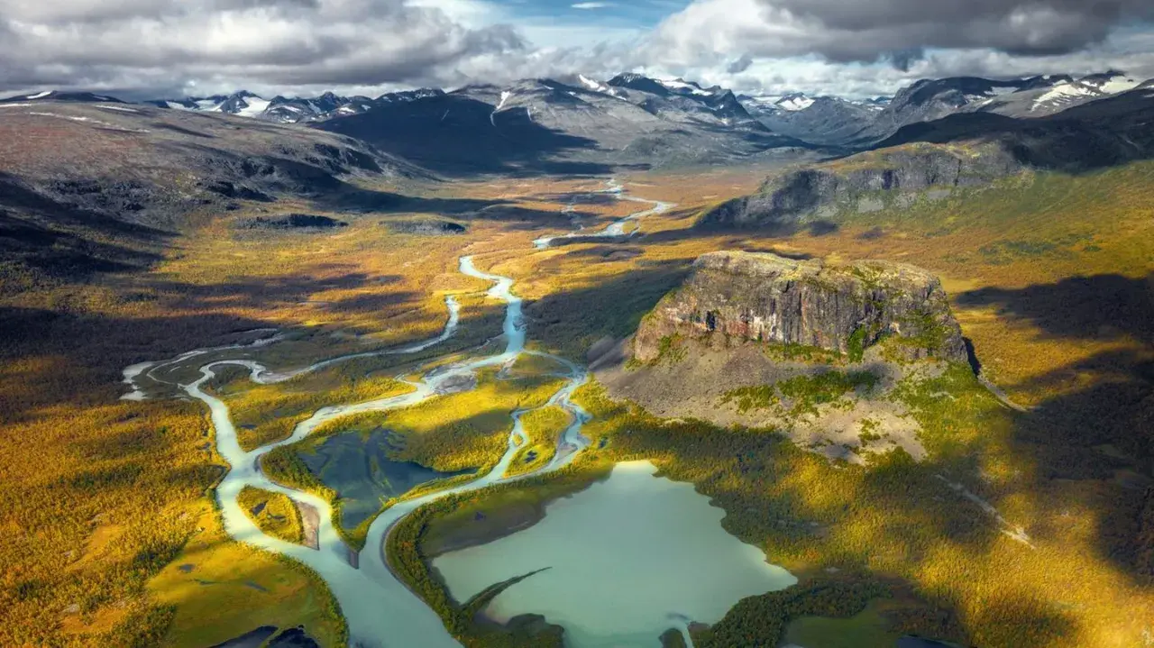 Weites Tal mit Fluss und Berg in Schwedens Nationalparks. Herbstliche Farben und dramatische Wolken über der Landschaft.