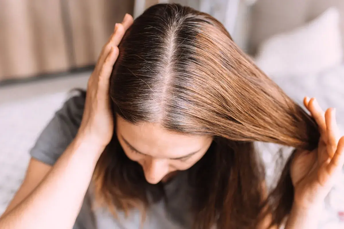 Una mujer se toca el cabello, mostrando mechones grises que explican porque salen canas.