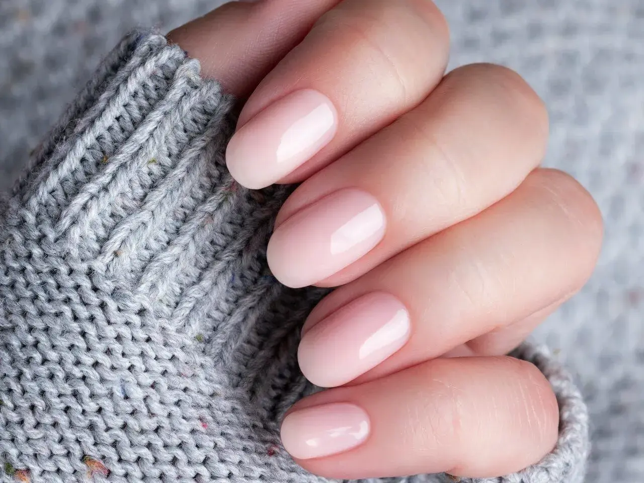 Dłoń z delikatnym, różowym manicure. Czy baza kauczukowa niszczy paznokcie? Zdjęcie sugeruje, że nie, jeśli jest stosowana prawidłowo.