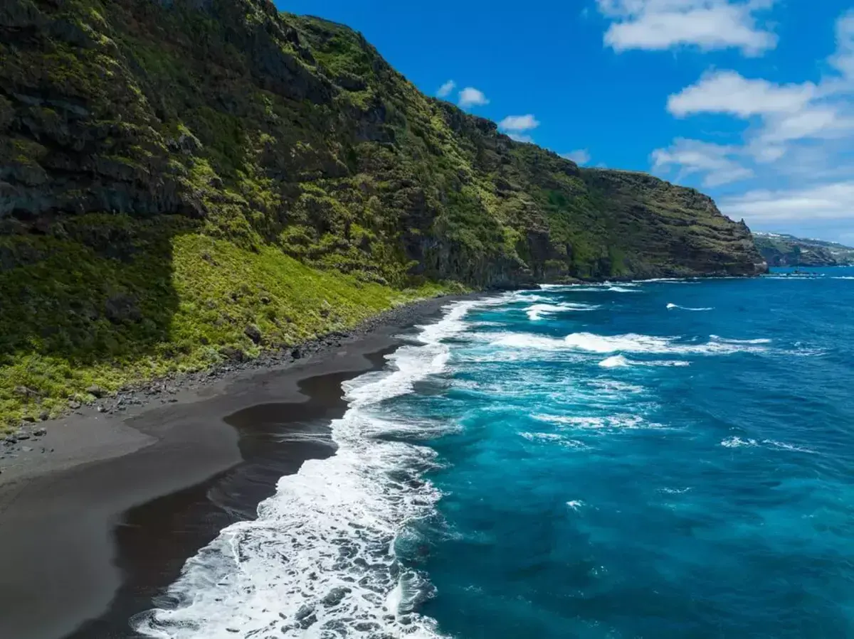 Costa salvaje con arena negra y mar azul intenso, un rincón idílico de las playas de Canarias.