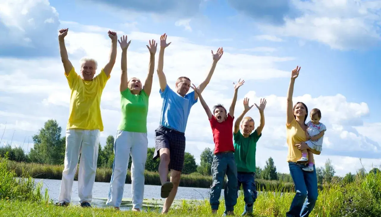 Familia disfrutando de actividades al aire libre, saltando y riendo junto a un lago.