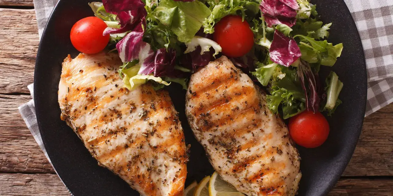 Due petti di pollo grigliati, conditi con erbe aromatiche, serviti con un'insalata fresca, pomodorini e spicchi di limone.