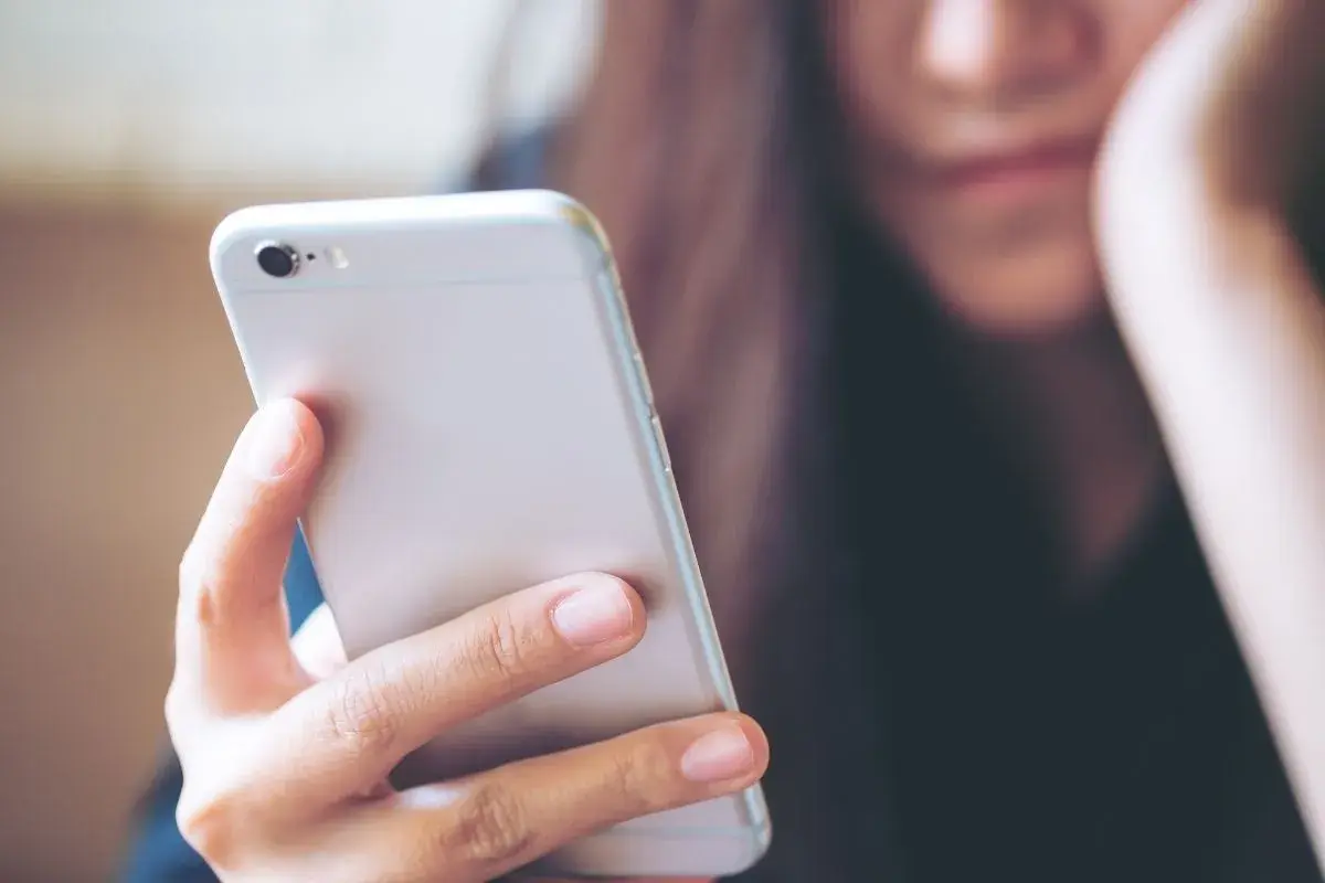 Kobieta trzyma telefon, zastanawiając się, jak wysłać mms.