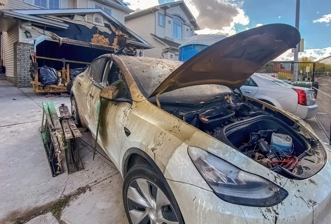 Spalony samochód elektryczny przed zniszczonym garażem. Może to być przyczyna, dlaczego w 2026 r. wzrosła liczba pożarów w warsztatach przez błędy w ładowaniu baterii.