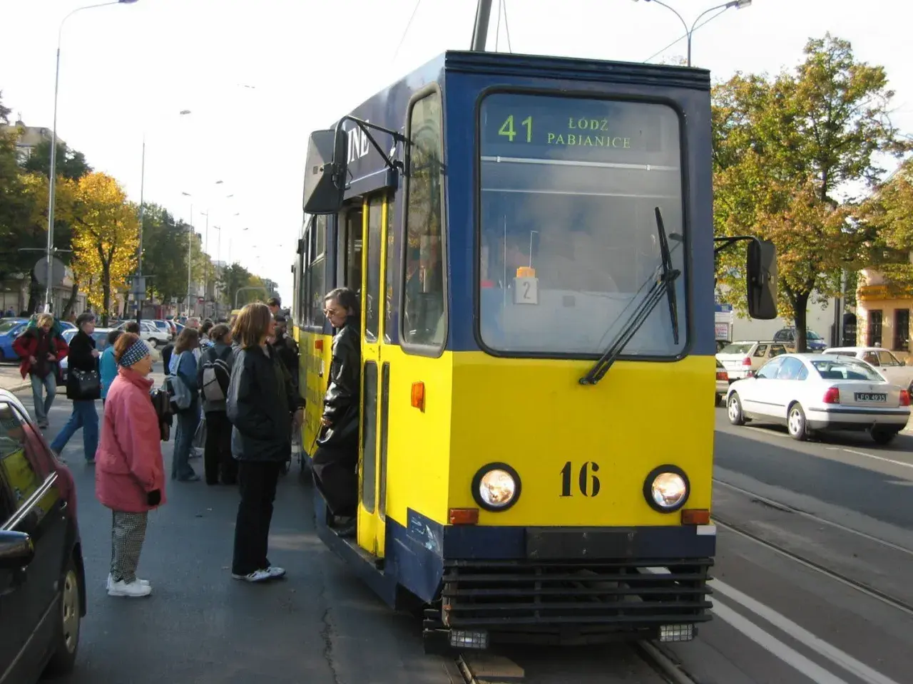 Żółto-niebieski tramwaj linii 41 Łódź Pabianice stoi na przystanku, czekając na pasażerów.