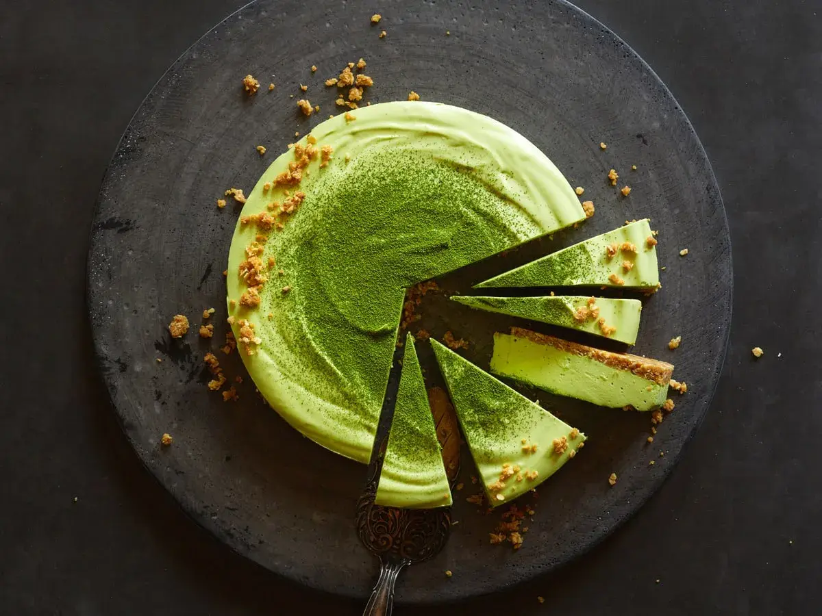 Ein köstliches Matcha-Dessert, in Stücke geschnitten, mit zerbröselten Keksen und feinem Matcha-Pulver bestreut.