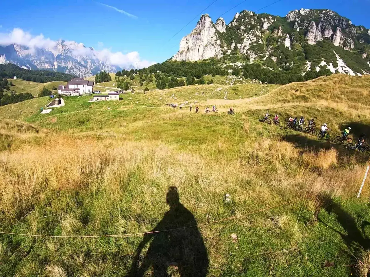 Gruppo di ciclisti in discesa su un sentiero erboso, con montagne imponenti sullo sfondo. Un'avventura a Recoaro 1000.
