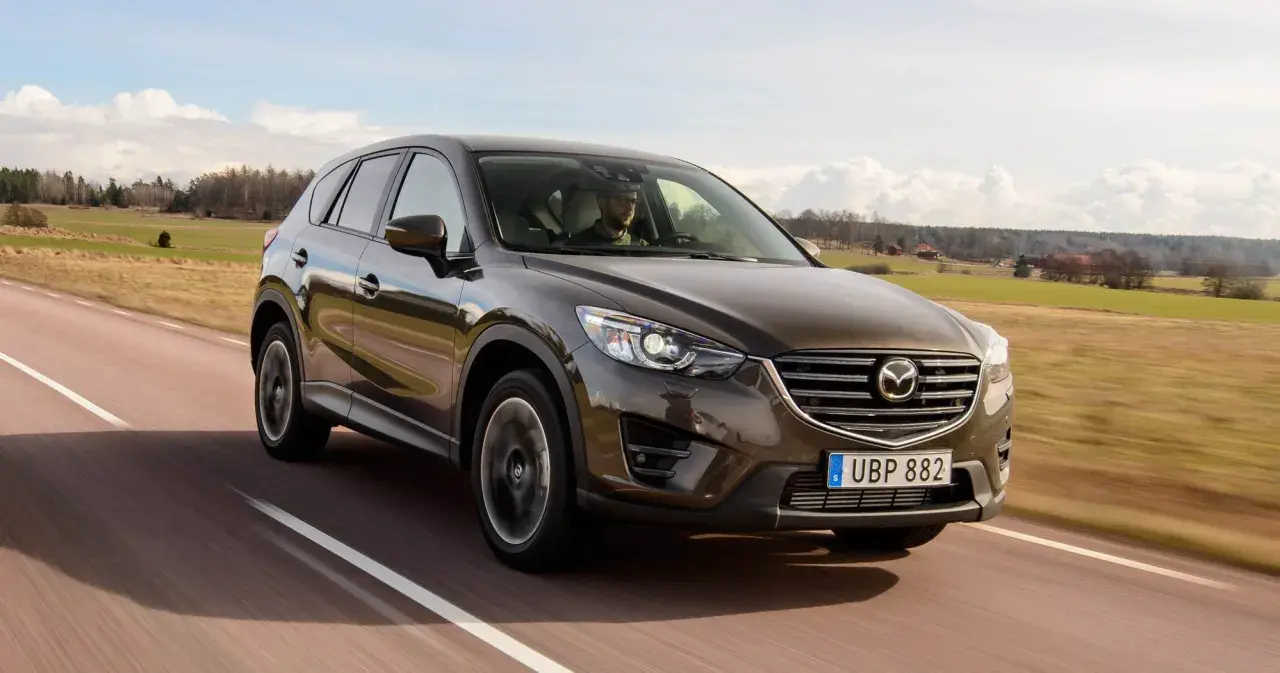 Brun Mazda CX-5 kör på en landsväg i Sverige. Föraren verkar ha ett problem med bilen.