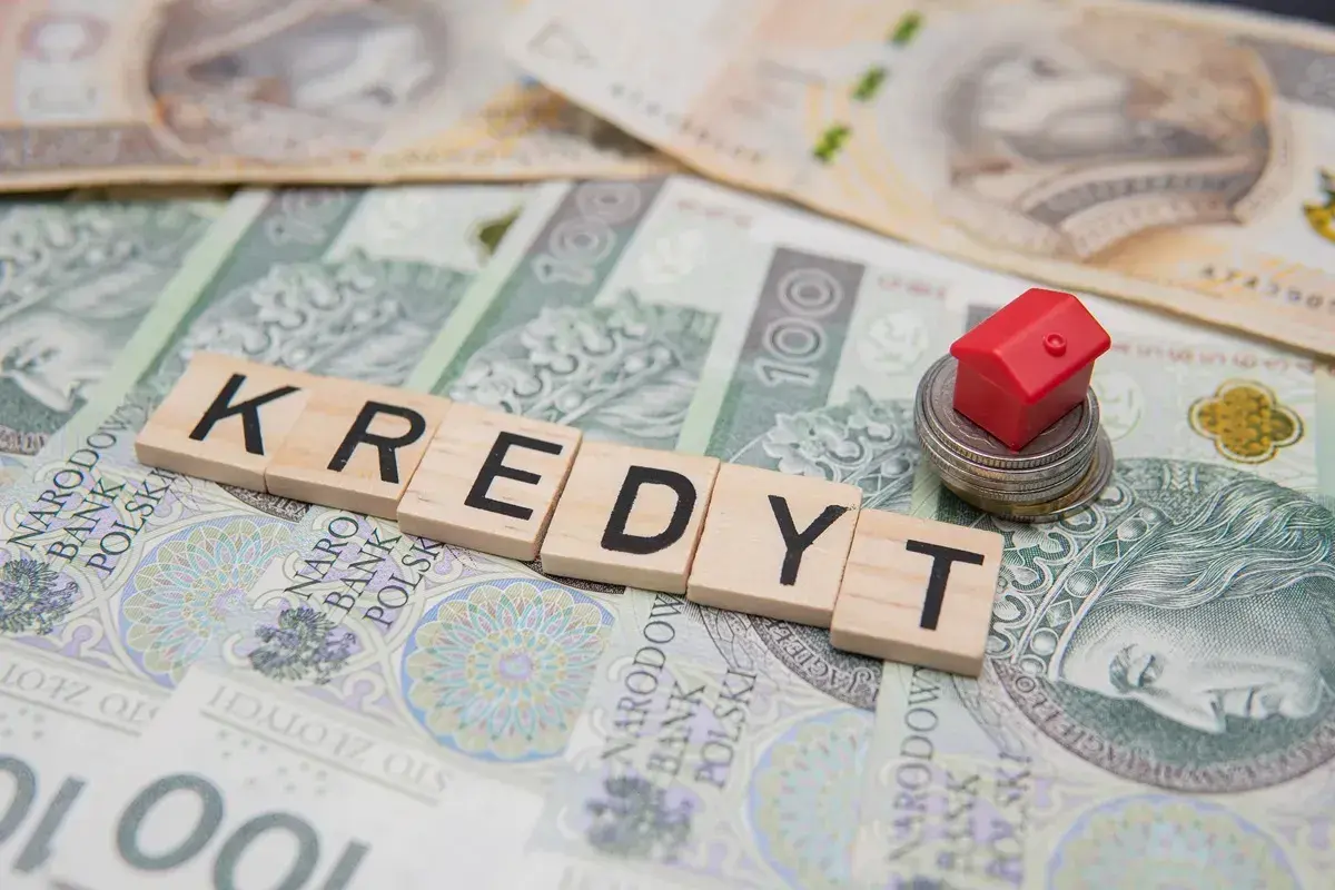 Kredyt 400 tys jaka rata? Mały czerwony domek na stosie monet i banknotów symbolizuje marzenie o własnym M.