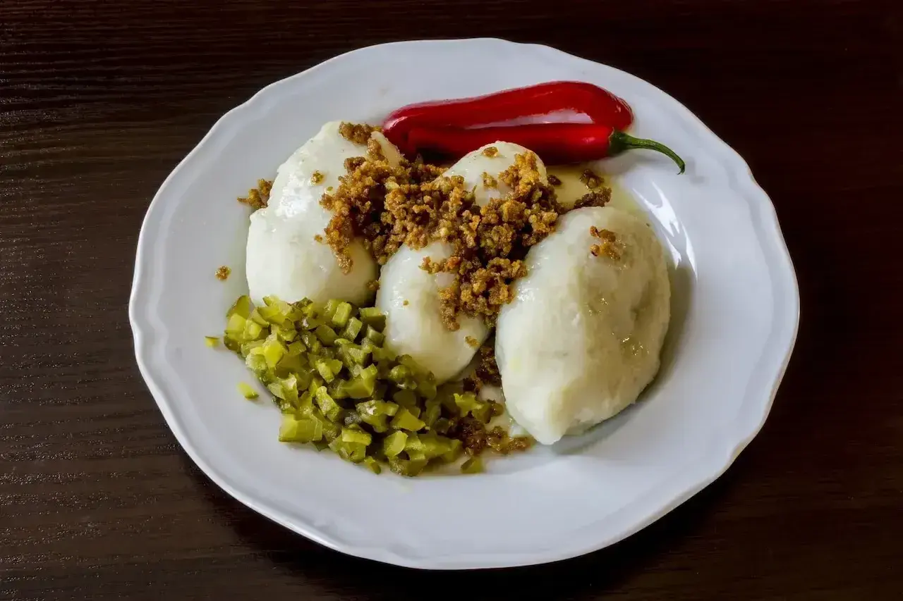 Trzy sycące kartacze z mięsem, posypane skwarkami, z dodatkiem ogórków kiszonych i papryczki chili.