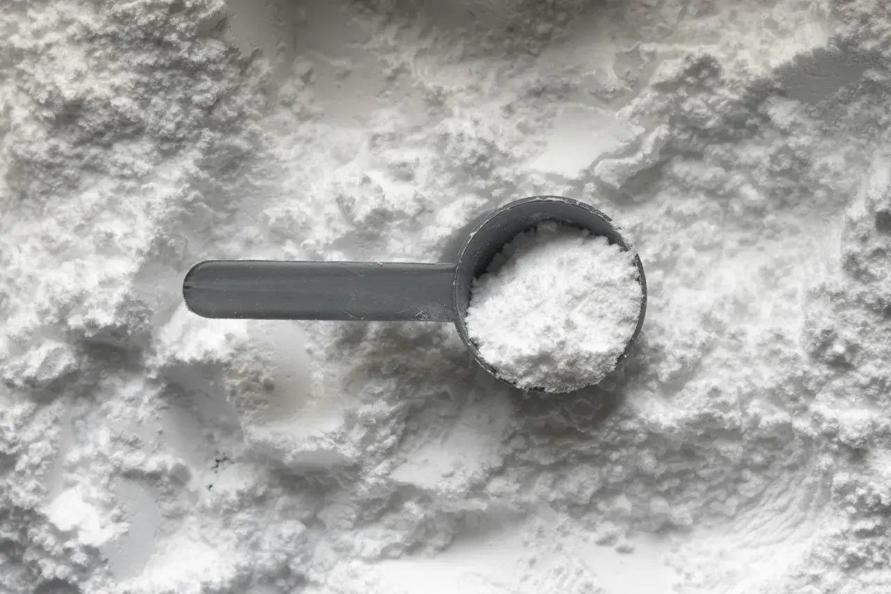 Miarka z białym proszkiem, prawdopodobnie disodium edta, na tle sypkiego materiału.