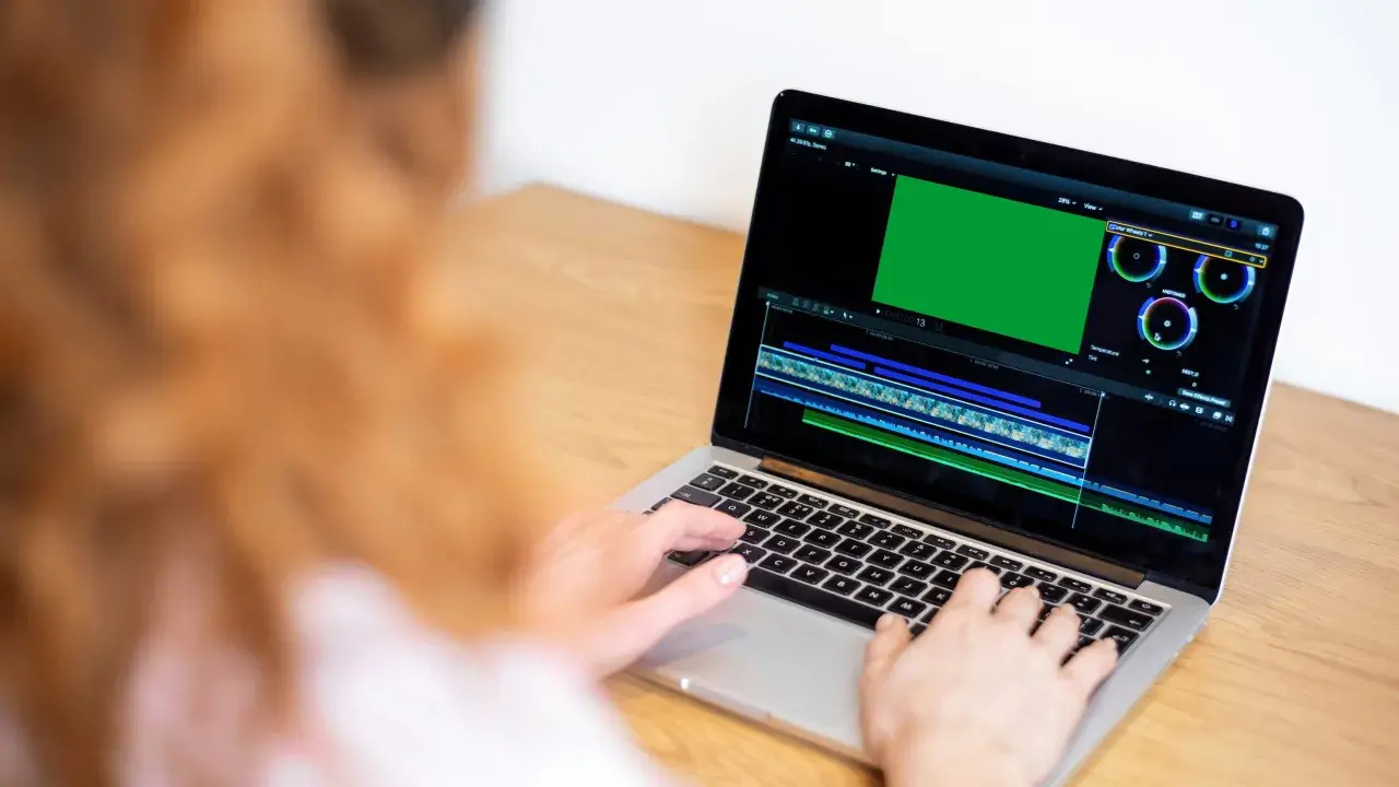 Osoba pracuje na laptopie, edytując wideo. Na ekranie widać zielony podgląd i oś czasu, co sugeruje, że uczy się, jak nagrywać ekran na laptopie.