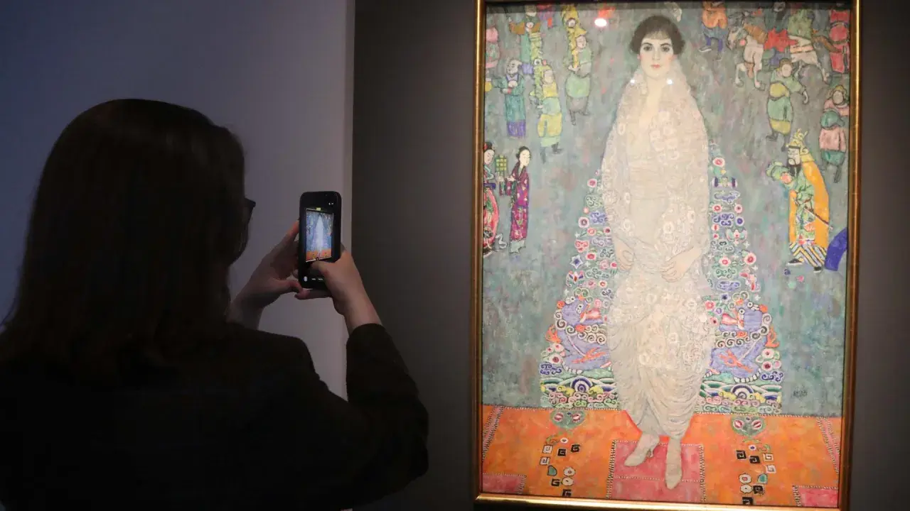 Besucherin fotografiert das größte Gemälde der Welt, ein detailreiches Porträt einer Frau in einem opulenten Kleid, umgeben von bunten Figuren.