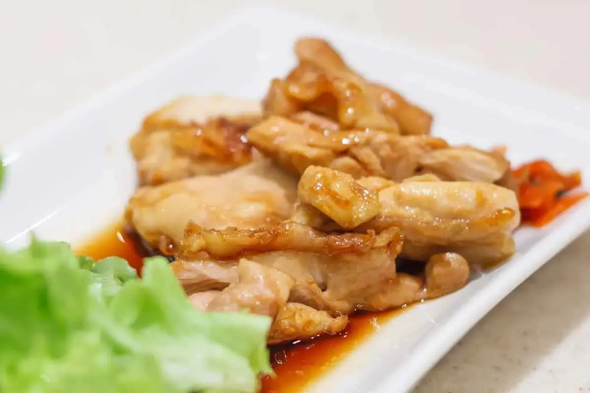 Straccetti di pollo succulenti e dorati, serviti su un piatto bianco con insalata fresca e carote sottaceto.