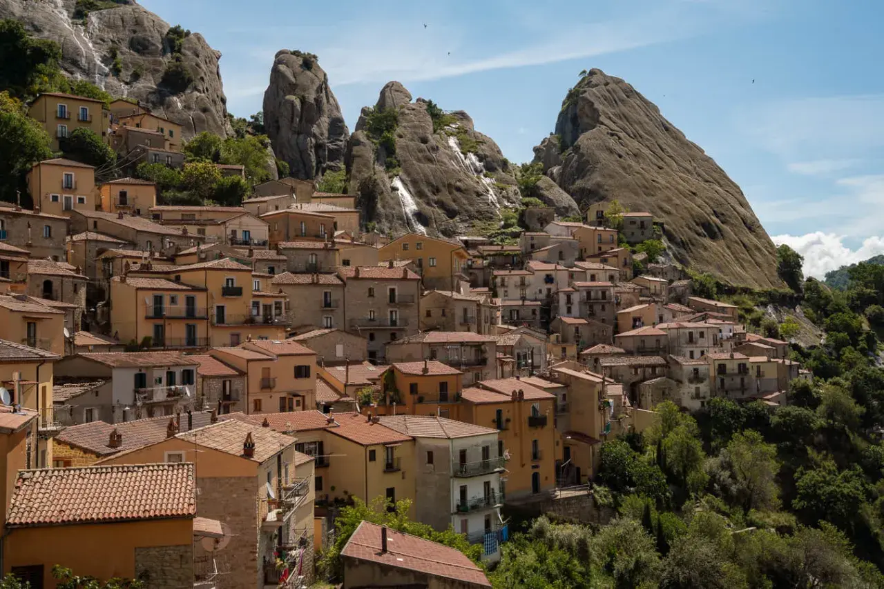 Houses cling to a mountainside in Pietrapertosa, Italy, beneath dramatic rock formations.