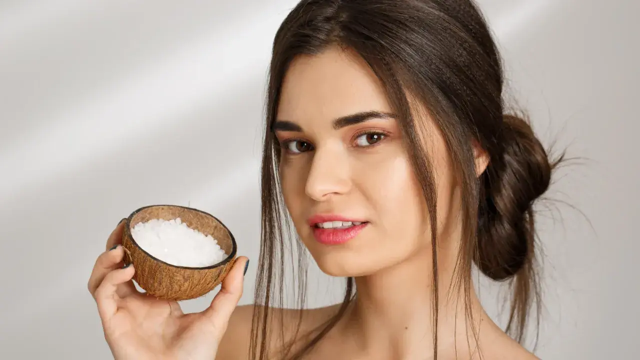 Mujer sonríe sosteniendo una cáscara de coco con gránulos blancos, ideal para el aceite de coco para el pelo.