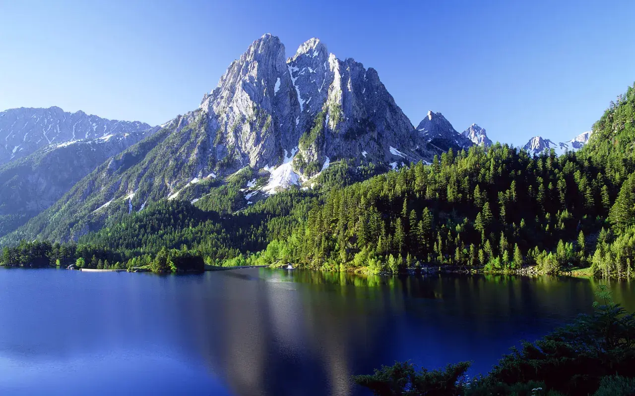 El estany de Sant Maurici, un lago alpino rodeado de bosques de pinos y picos nevados, refleja la majestuosidad de la naturaleza.