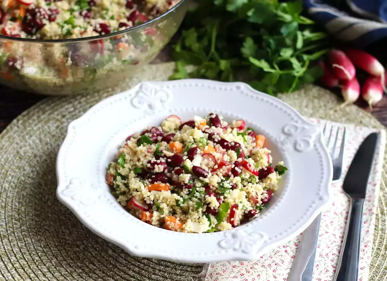 En härlig couscous sallad med bönor, morötter och rädisor, serverad på en vit tallrik.