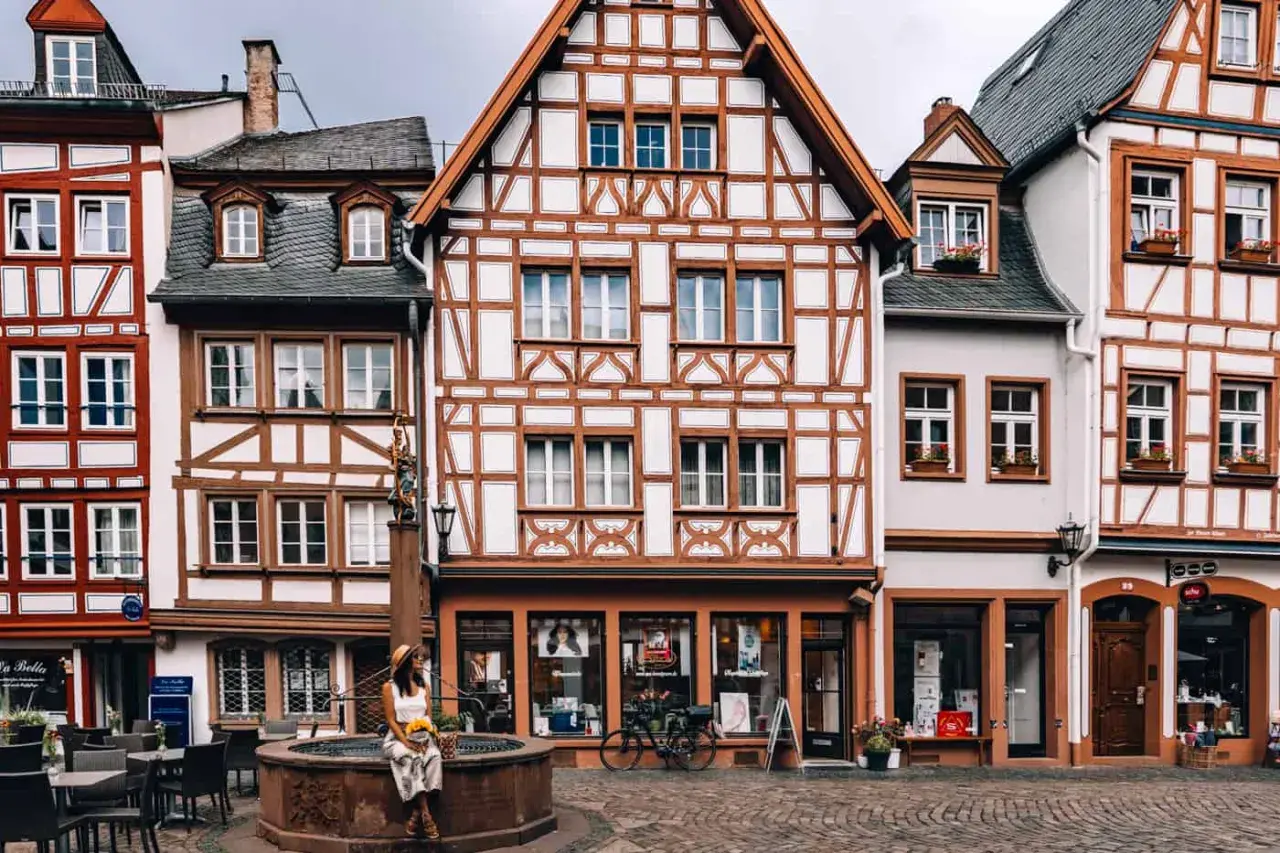 Fachwerkhaus-Idylle in Mainz. Eine Frau sitzt am Brunnen, umgeben von malerischen Gassen – hier sind die echten Mainz Geheimtipps!