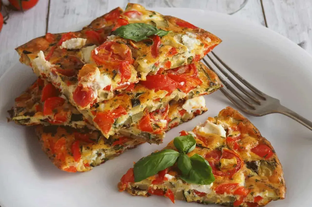 Une part d'omelette aux légumes colorée, garnie de tomates, courgettes et fromage frais, avec une feuille de basilic.