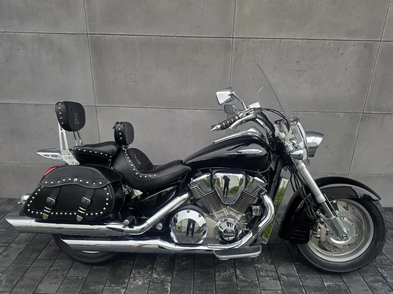 Czarny motocykl Honda VTX 1800 Neo z sakwami i oparciem dla pasażera, lśniący chromem na tle szarej ściany.