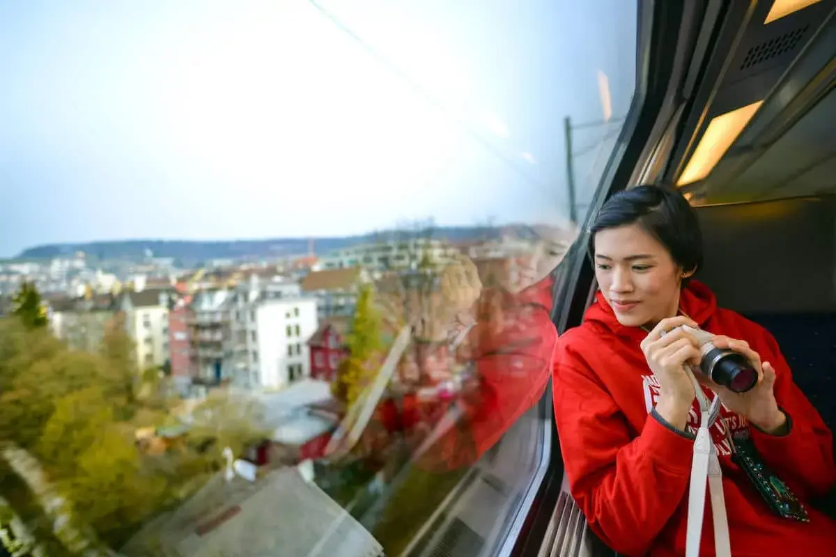 Joven en tren, con cámara, mirando el paisaje urbano. Quizás viajando en un tren de Tarragona a Sevilla.