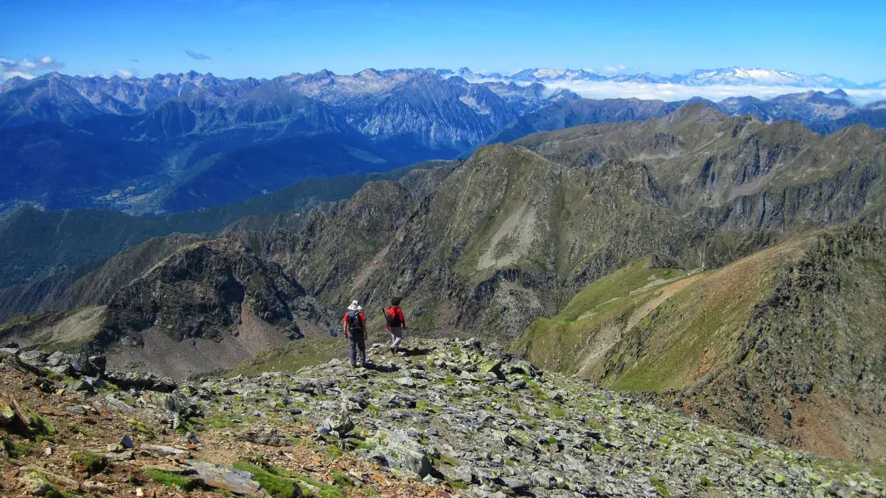 Dos excursionistas exploran las impresionantes **rutas de Esterri d'Àneu**, rodeados de picos montañosos y un cielo azul.