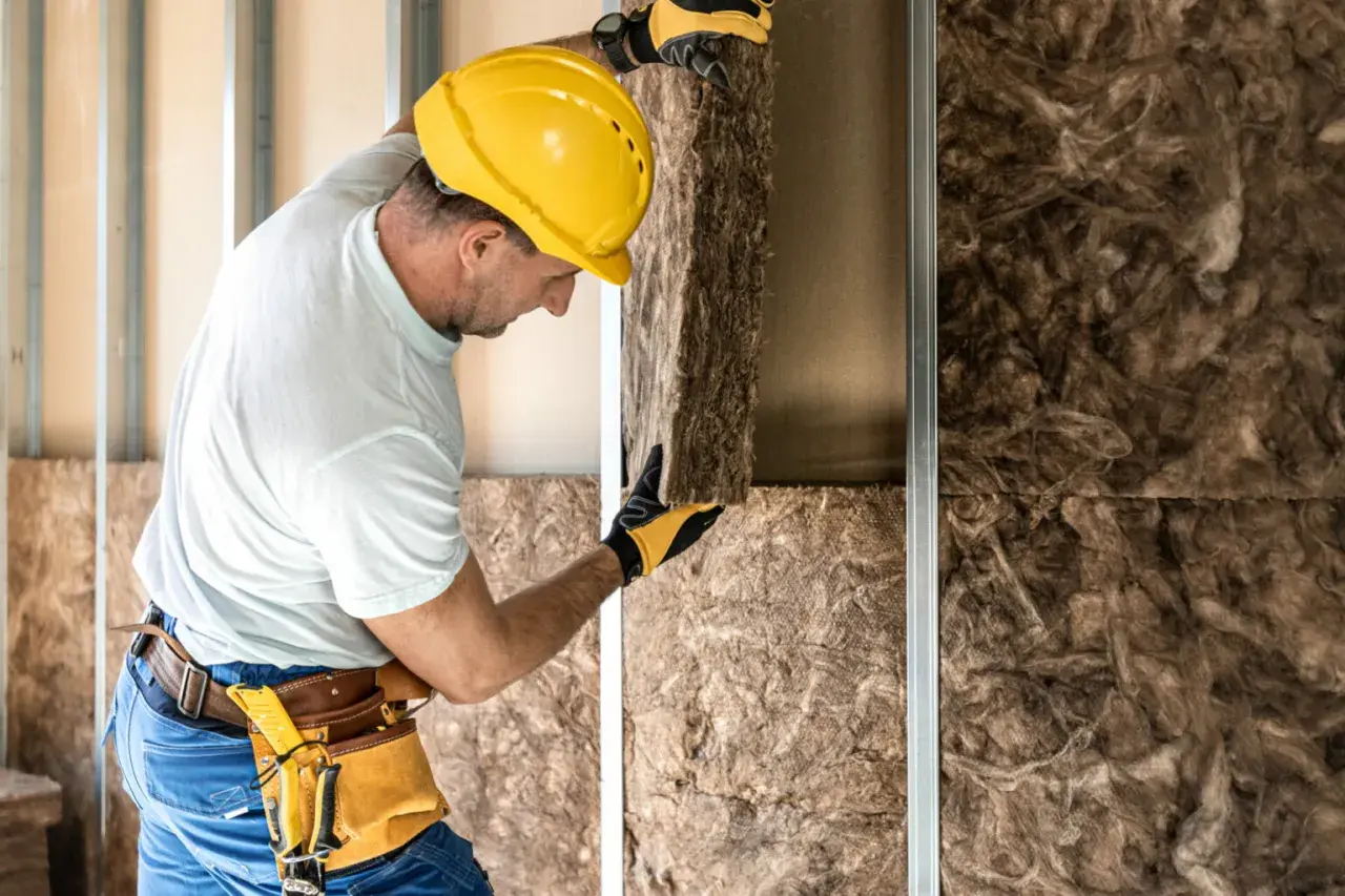 Operaio con casco giallo installa pannelli per l'isolamento acustico in una parete in costruzione.