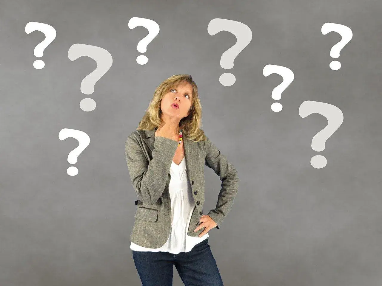 Kobieta zamyślona otoczona znakami zapytania.