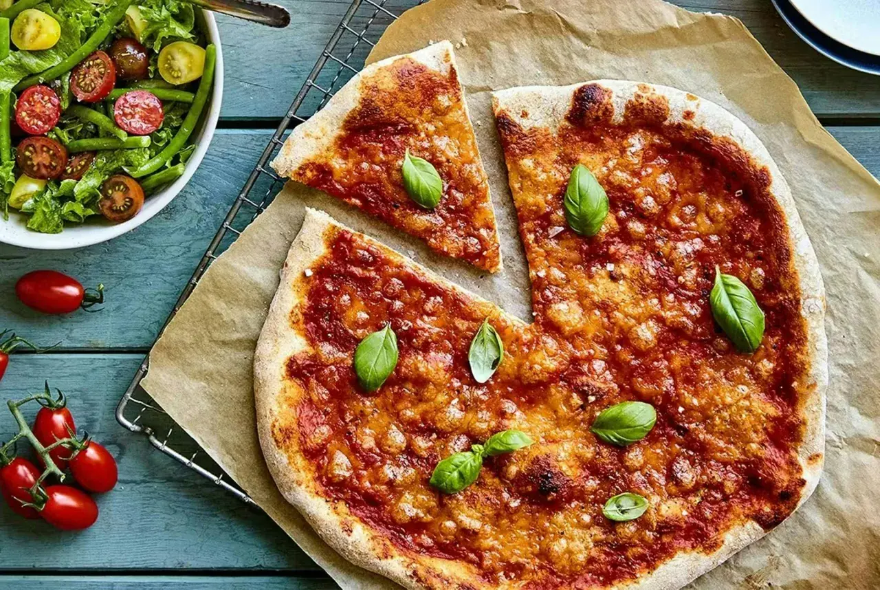 En saftig vegetarisk pizza med tomatsås och ost, toppad med färsk basilika. Bredvid en fräsch sallad med gröna bönor och körsbärstomater.