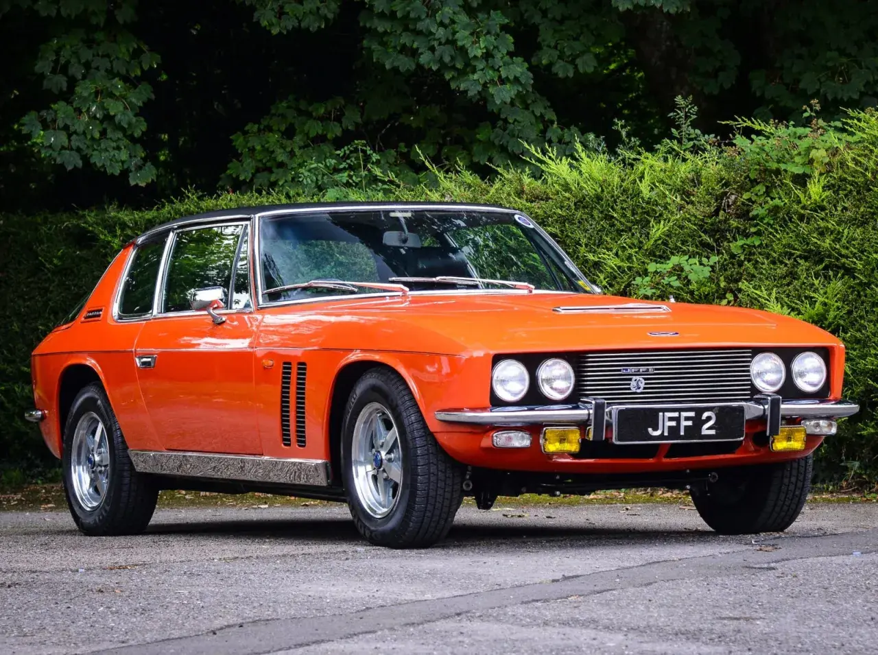En orange Jensen Interceptor från 70-talet, en klassisk bil med en tidlös design, parkerad utomhus.