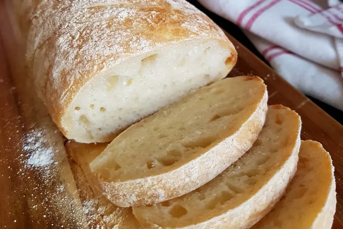 Frisch gebackenes ciabatta brot mit knuspriger Kruste und luftiger Krume, auf einem Holzbrett mit etwas Mehl bestäubt.