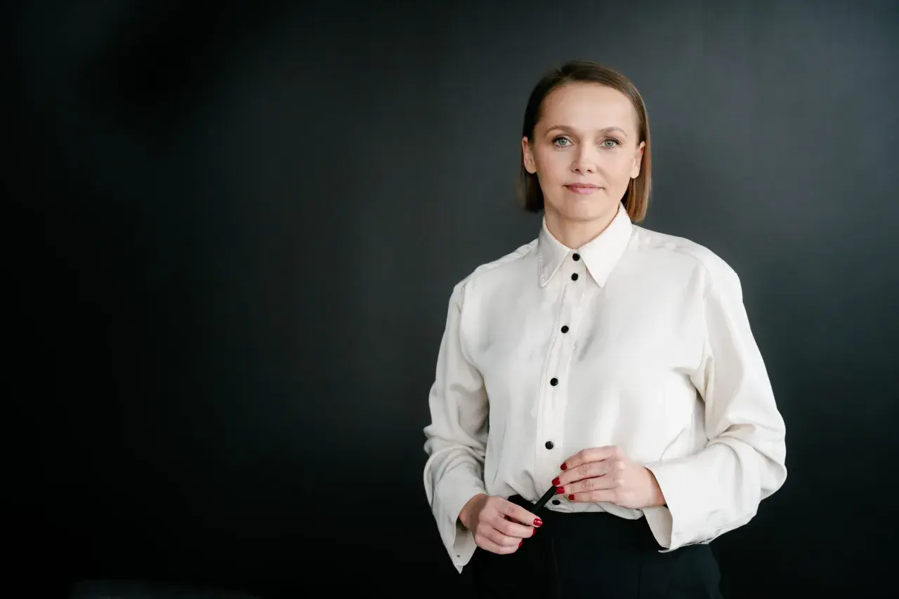 Kobieta w białej koszuli i czarnych spodniach na ciemnym tle.