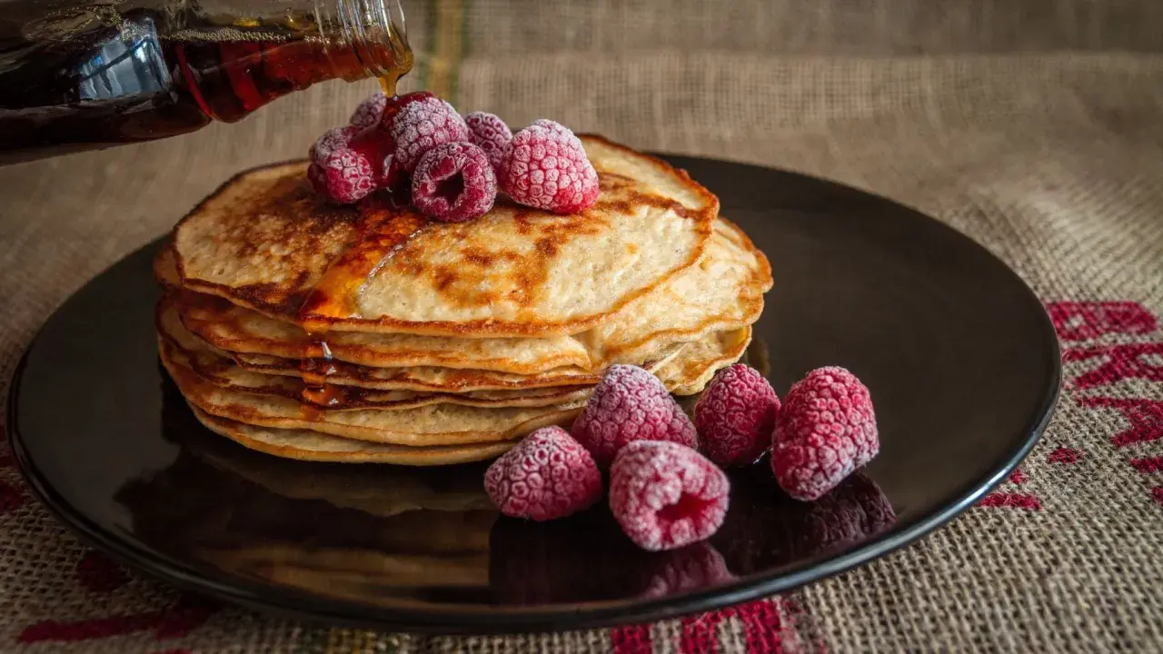Pila de tortitas doradas con frambuesas congeladas y sirope cayendo. Una deliciosa receta de tortitas para disfrutar.