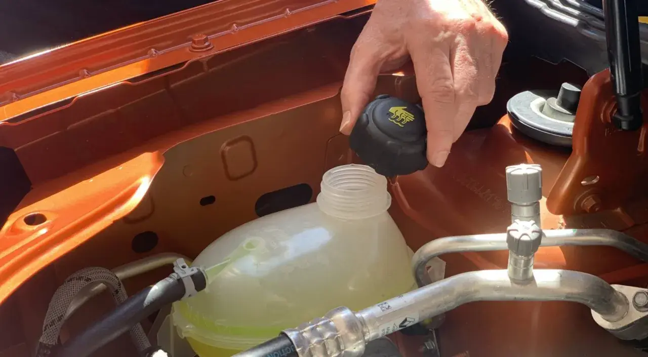 Mano quitando el tapón del depósito de anticongelante, que parece bajo. El anticongelante se evapora con el tiempo.