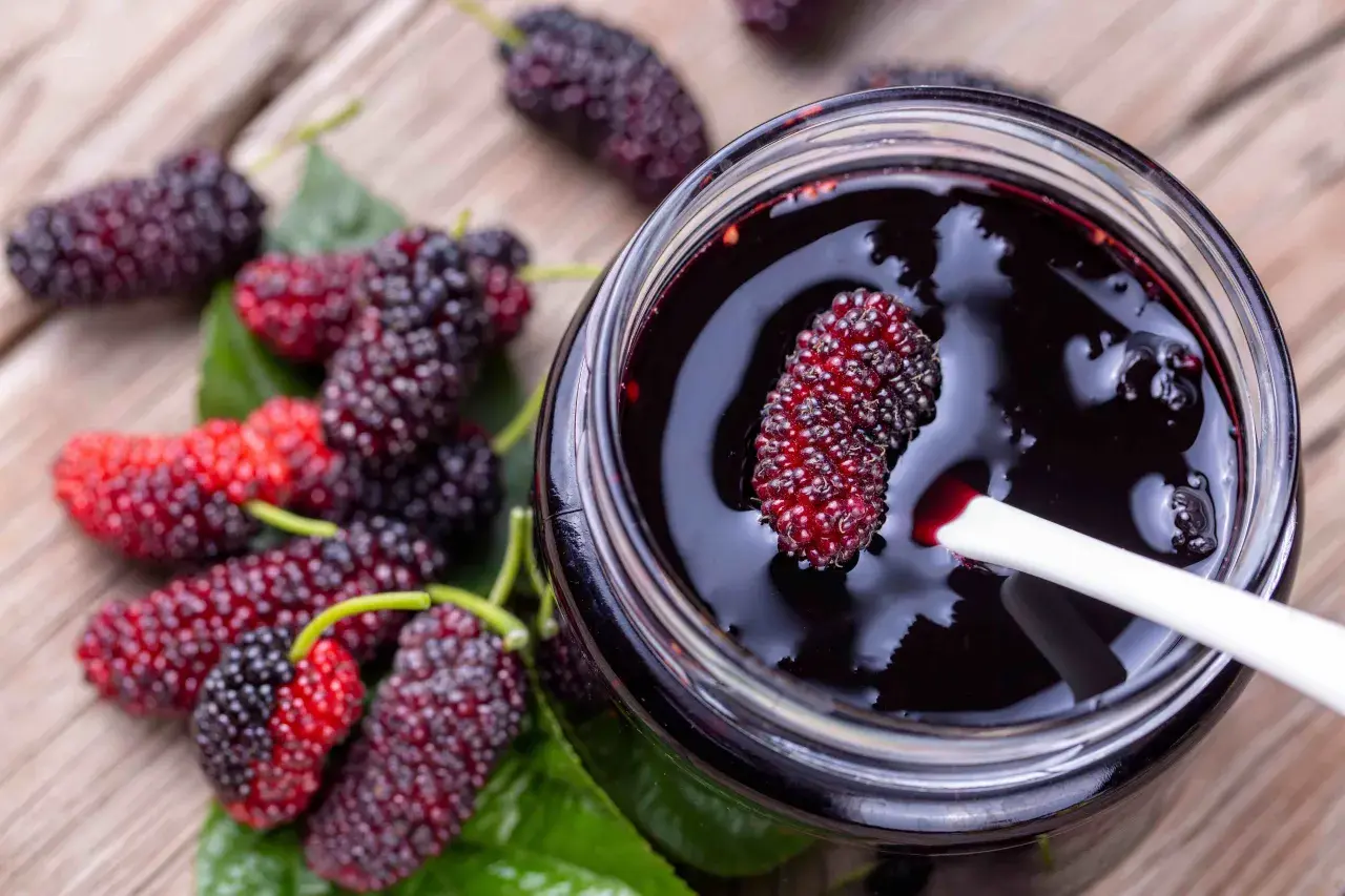 Un vasetto di marmellata di gelso frutto, con alcuni frutti freschi sparsi sul tavolo di legno.