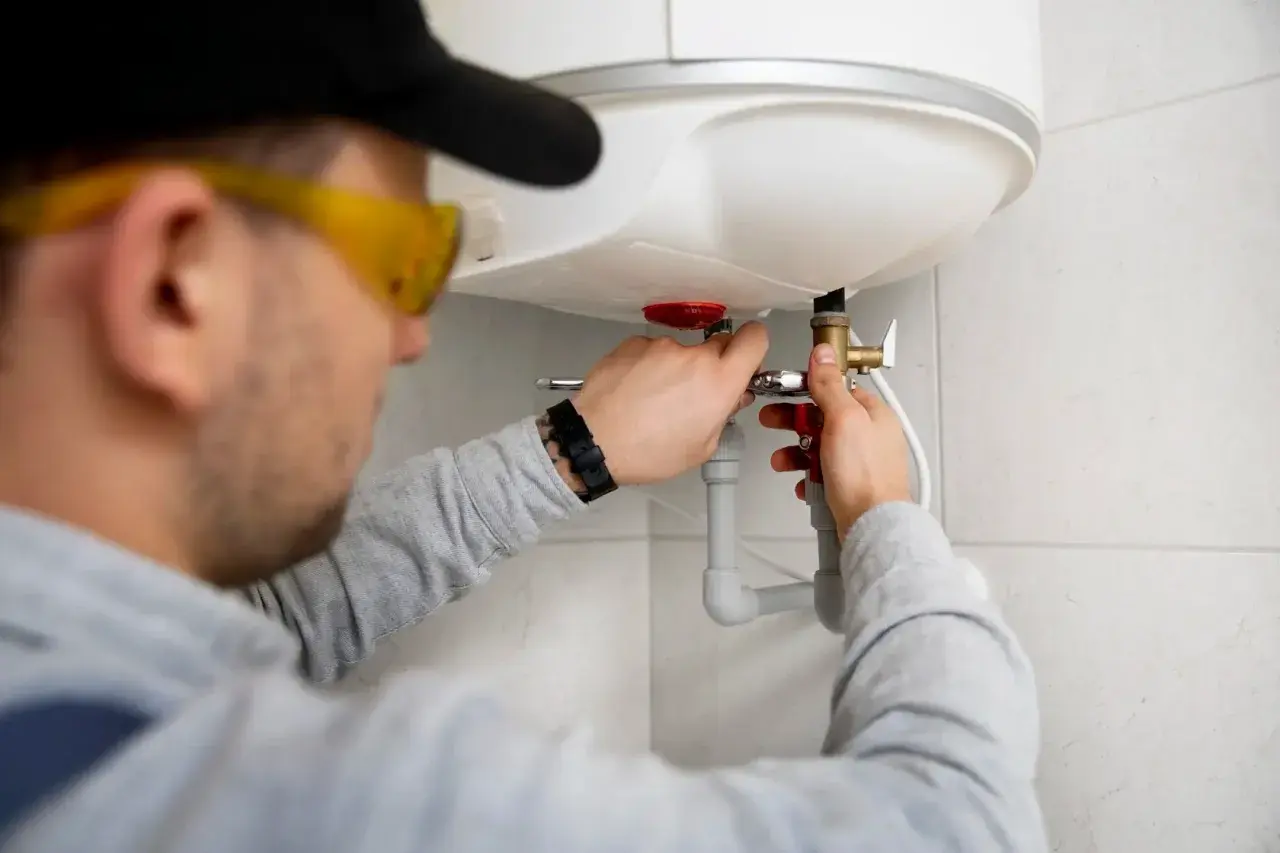 Fachowiec w okularach ochronnych dokonuje montażu bojlera elektrycznego, podłączając instalację wodną.