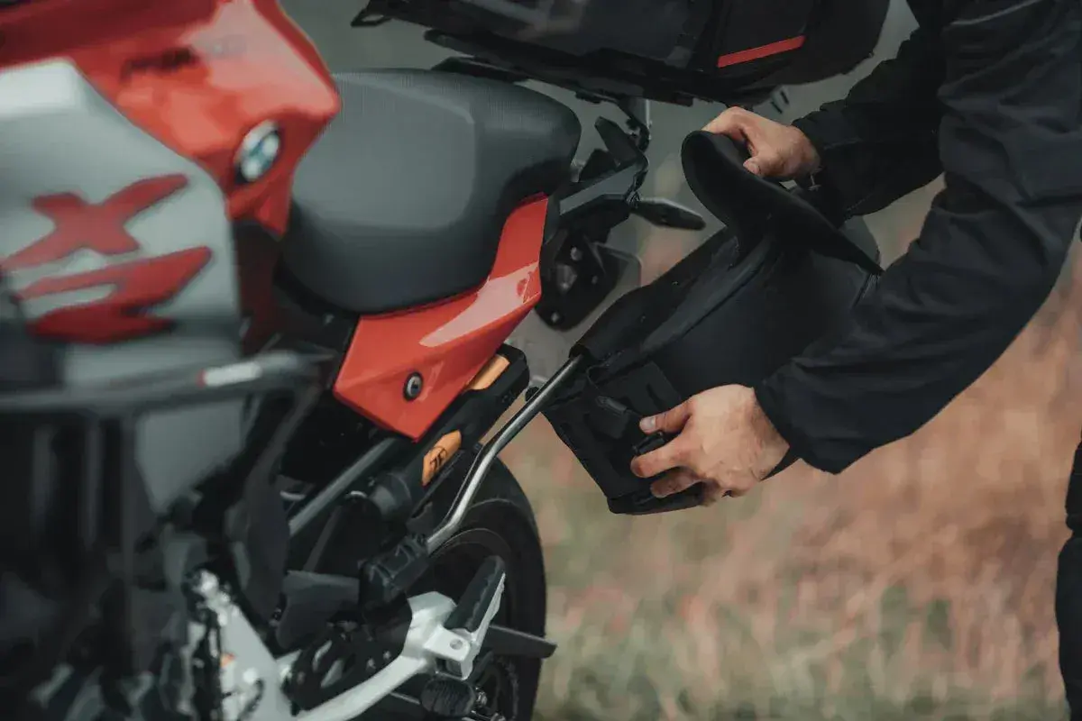 Mężczyzna montuje czarną sakwę motocyklową do czerwonego motocykla.