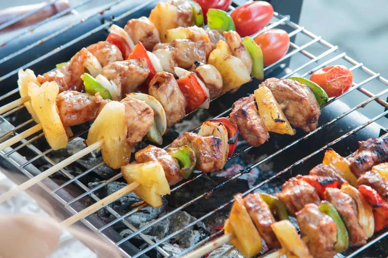Na grillu piecze się kilka szaszłyków z kurczakiem, ananasem, papryką i pomidorkami.