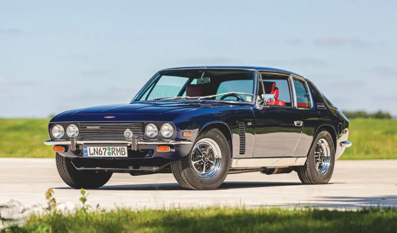 Mörkblå Jensen Interceptor med röda säten, parkerad utomhus på en solig dag.